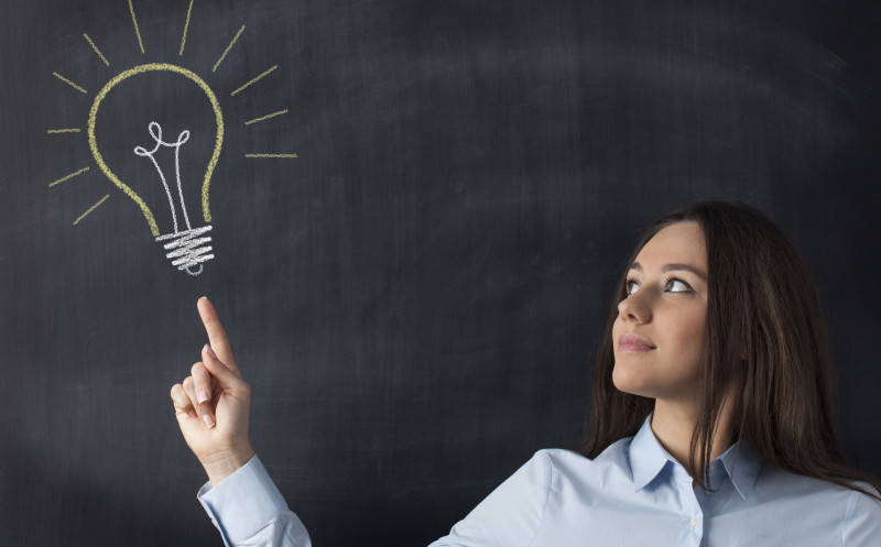 Big glowing light bulb on blackboard with businesswoman hand pointing it