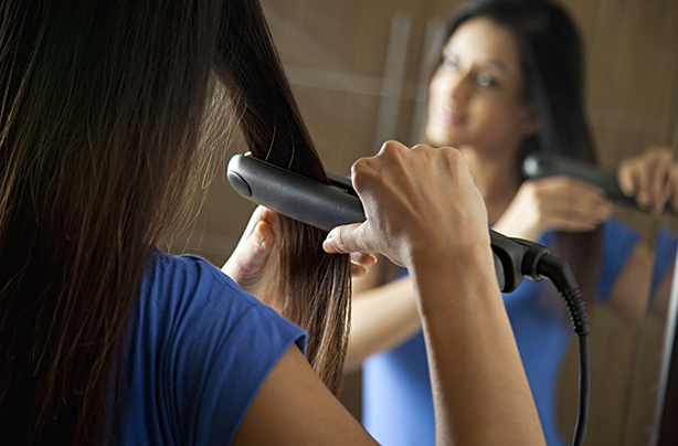 Young woman using hair straightener